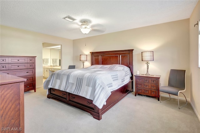 bedroom with ceiling fan, light colored carpet, a textured ceiling, and ensuite bath