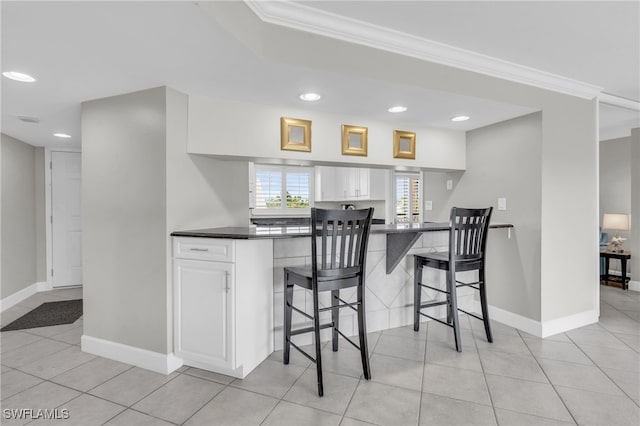 kitchen with white cabinets, light tile patterned floors, ornamental molding, kitchen peninsula, and a breakfast bar