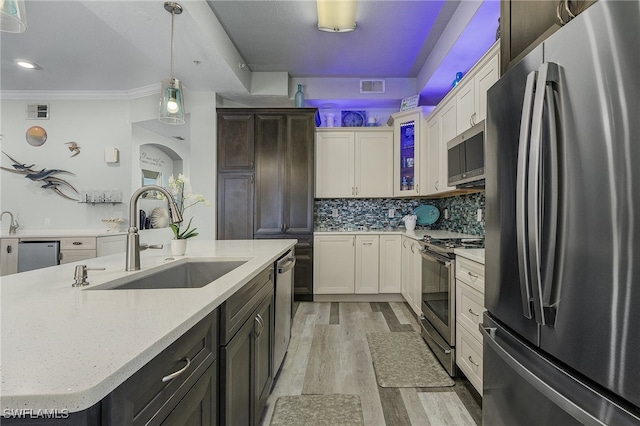 kitchen with hanging light fixtures, light wood-type flooring, stainless steel appliances, sink, and a center island with sink