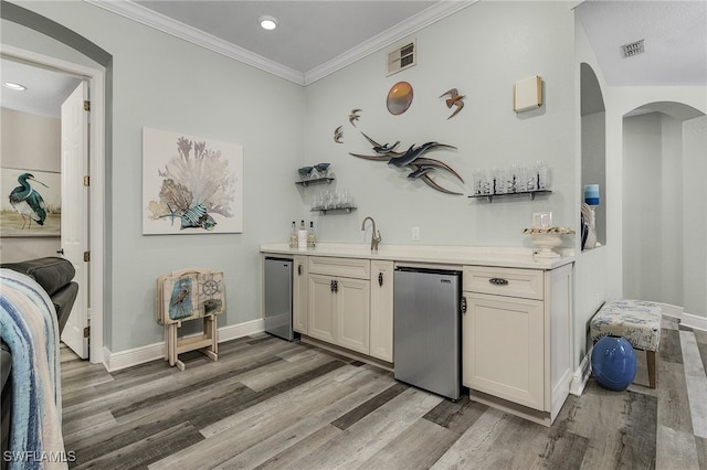 bar with light wood-type flooring, ornamental molding, stainless steel refrigerator, and sink