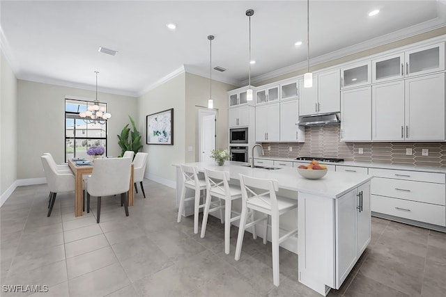 kitchen with an inviting chandelier, stainless steel appliances, white cabinetry, pendant lighting, and a center island with sink