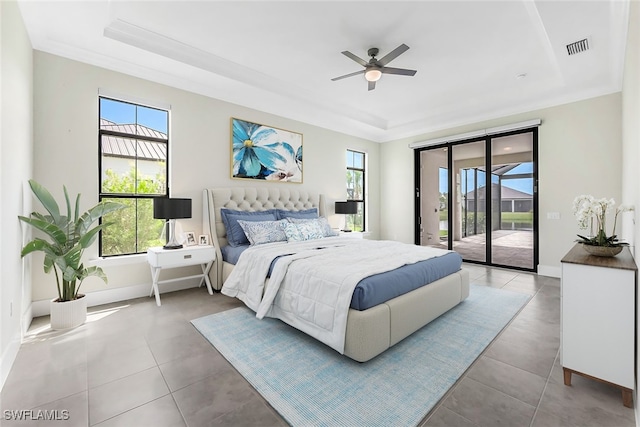 tiled bedroom with multiple windows, ceiling fan, a tray ceiling, and access to exterior