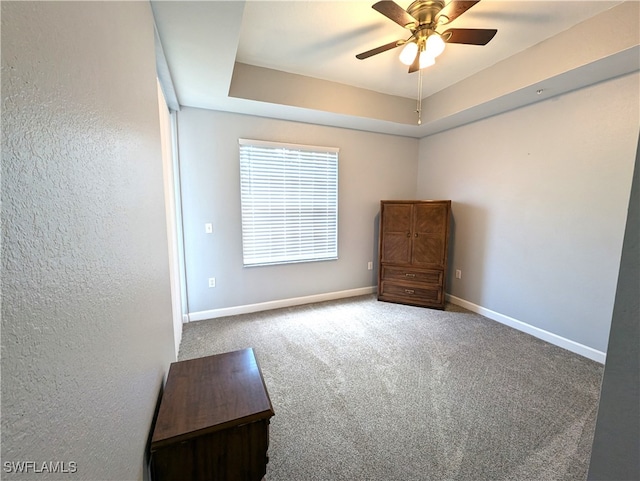 unfurnished bedroom featuring a raised ceiling, ceiling fan, and carpet flooring