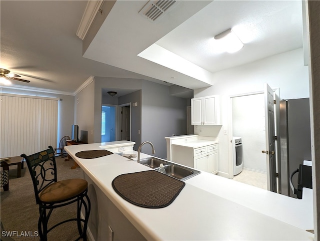 kitchen with washer / clothes dryer, a kitchen bar, sink, white cabinetry, and ceiling fan