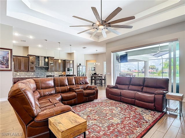 living room featuring ceiling fan with notable chandelier, a tray ceiling, and light hardwood / wood-style flooring