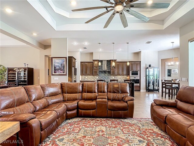 living room with a tray ceiling, ceiling fan with notable chandelier, and light wood-type flooring