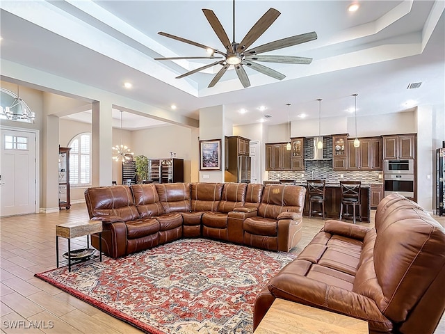 living room featuring a tray ceiling, light hardwood / wood-style flooring, a high ceiling, and ceiling fan with notable chandelier