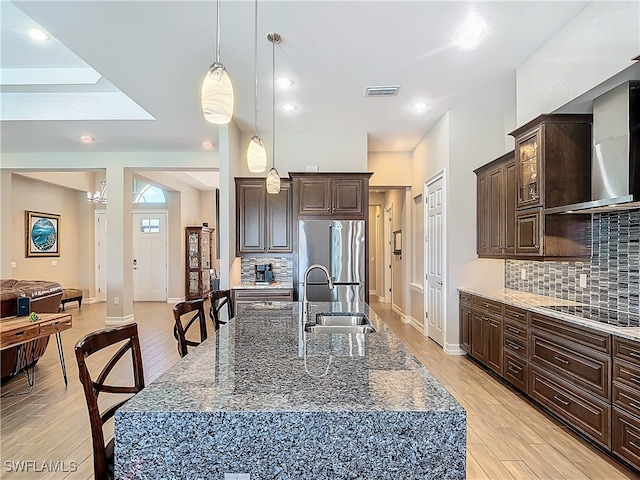 kitchen featuring cooktop, light wood-type flooring, a kitchen island with sink, and stainless steel refrigerator