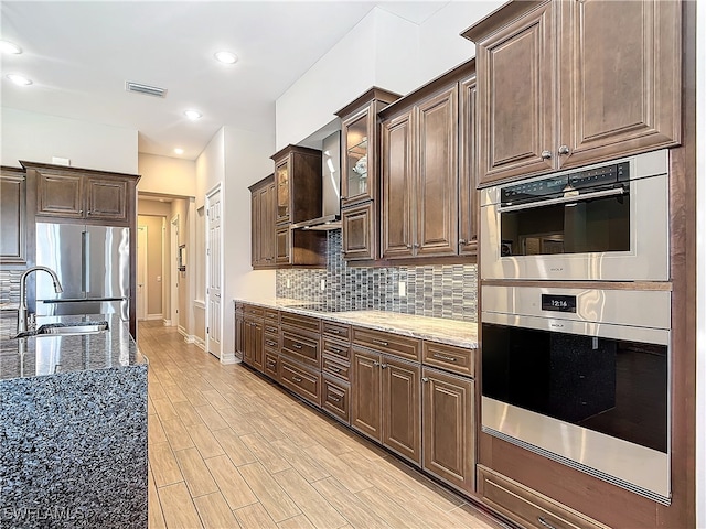 kitchen featuring dark brown cabinets, stainless steel appliances, sink, dark stone countertops, and light hardwood / wood-style floors