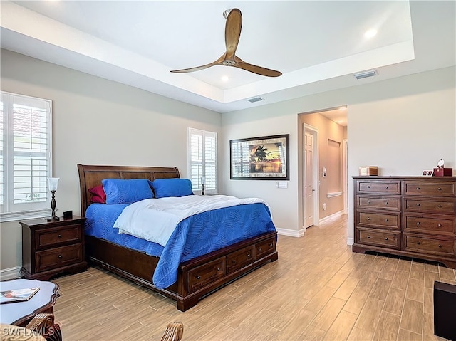 bedroom with a raised ceiling, ceiling fan, ensuite bathroom, and light hardwood / wood-style floors