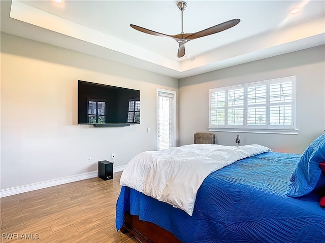 bedroom with hardwood / wood-style floors, a raised ceiling, and ceiling fan