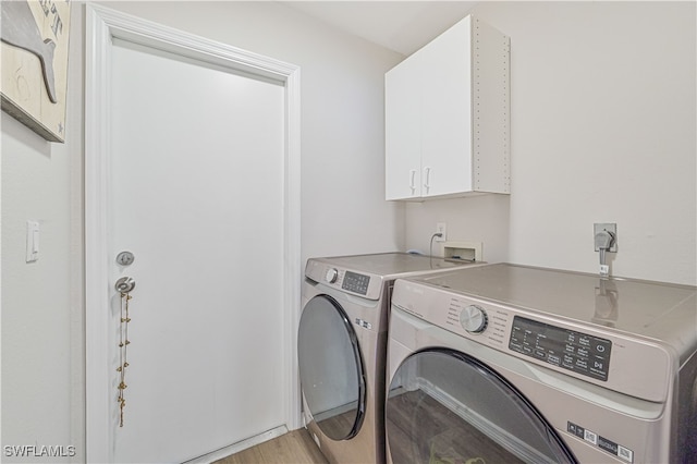 laundry room with washing machine and clothes dryer, cabinets, and light hardwood / wood-style flooring