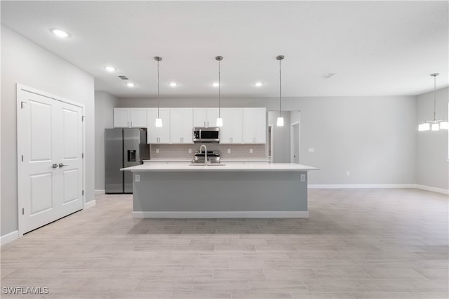 kitchen featuring an island with sink, hanging light fixtures, stainless steel appliances, and white cabinets