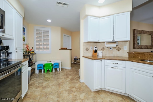 kitchen featuring dark stone counters, appliances with stainless steel finishes, white cabinetry, and decorative backsplash