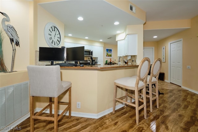 kitchen featuring white cabinetry, hardwood / wood-style flooring, a kitchen bar, and kitchen peninsula