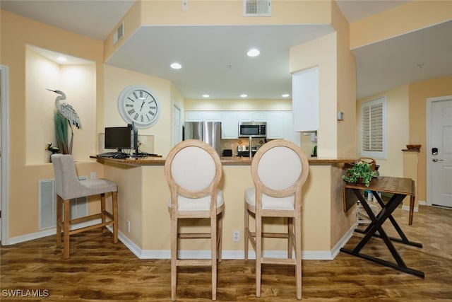 kitchen featuring kitchen peninsula, appliances with stainless steel finishes, dark hardwood / wood-style flooring, and a breakfast bar area