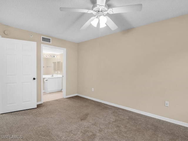 unfurnished bedroom with ceiling fan, light colored carpet, ensuite bathroom, and a textured ceiling