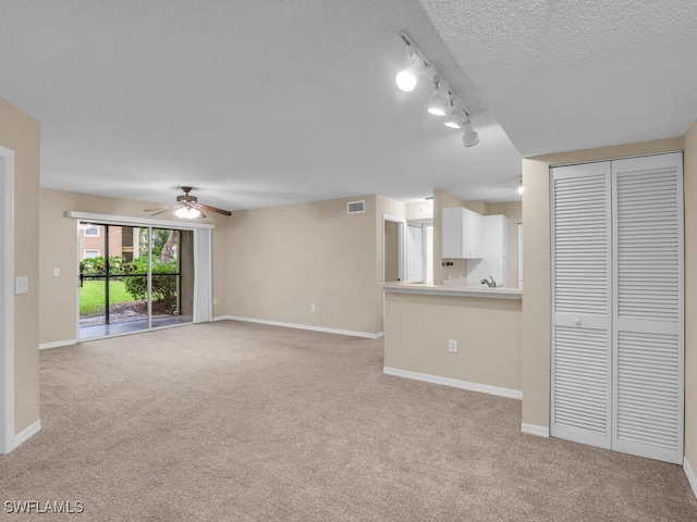 unfurnished living room featuring rail lighting, ceiling fan, light colored carpet, and a textured ceiling