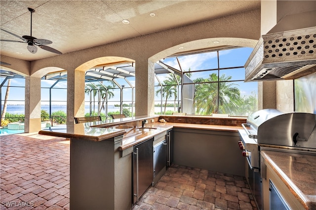 view of patio with a water view, exterior kitchen, sink, ceiling fan, and glass enclosure