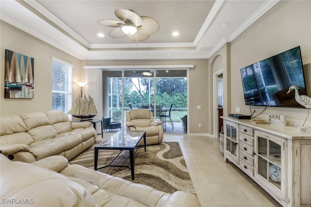 living area with light tile patterned floors, baseboards, ceiling fan, a tray ceiling, and crown molding