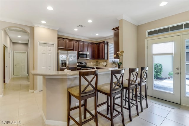 kitchen with light tile patterned floors, a peninsula, stainless steel appliances, light countertops, and a kitchen bar