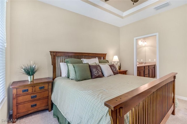 bedroom featuring visible vents, connected bathroom, light colored carpet, a tray ceiling, and a sink