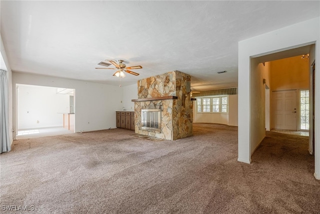 unfurnished living room with plenty of natural light, ceiling fan, a stone fireplace, and carpet