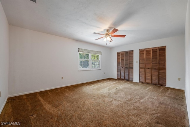 unfurnished bedroom with carpet, ceiling fan, and two closets