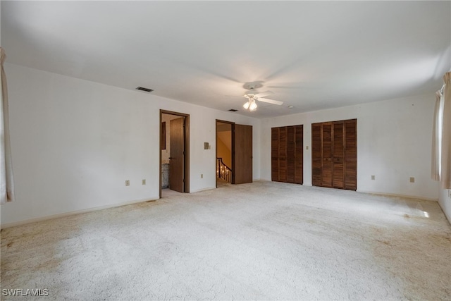 unfurnished bedroom with light colored carpet, ceiling fan, and two closets