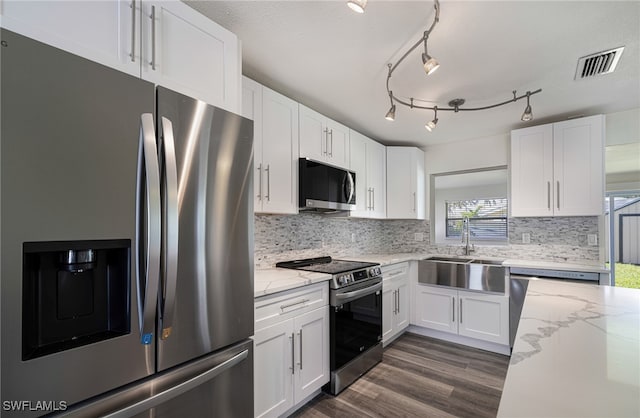 kitchen with appliances with stainless steel finishes, backsplash, light stone counters, sink, and white cabinetry