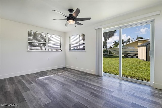 empty room featuring a healthy amount of sunlight, dark wood-type flooring, baseboards, and ceiling fan