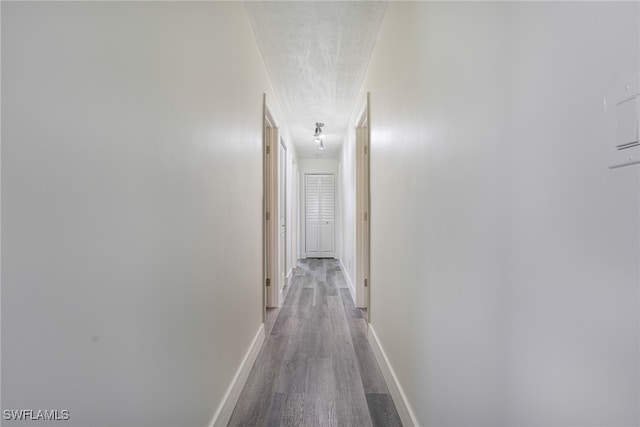 hallway with a textured ceiling, baseboards, and wood finished floors