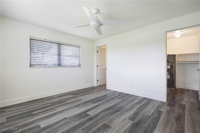 unfurnished bedroom featuring baseboards, dark wood-type flooring, a spacious closet, a textured ceiling, and electric water heater