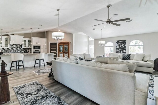 living room with hardwood / wood-style flooring, lofted ceiling, and ceiling fan with notable chandelier