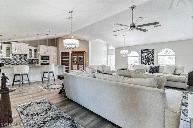 living area featuring ceiling fan with notable chandelier, vaulted ceiling, wood finished floors, and visible vents