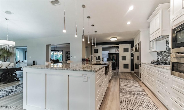 kitchen with a large island with sink, pendant lighting, white cabinets, and light hardwood / wood-style flooring