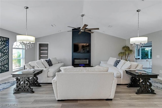 living room with lofted ceiling, ceiling fan with notable chandelier, a large fireplace, and light wood-type flooring