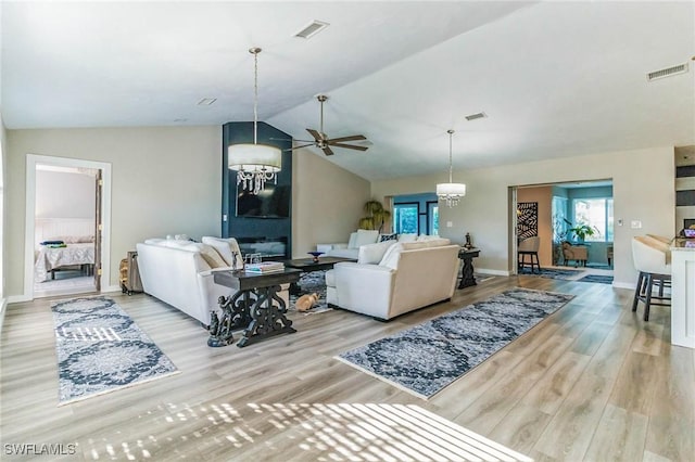 living room with ceiling fan with notable chandelier, light hardwood / wood-style floors, and lofted ceiling