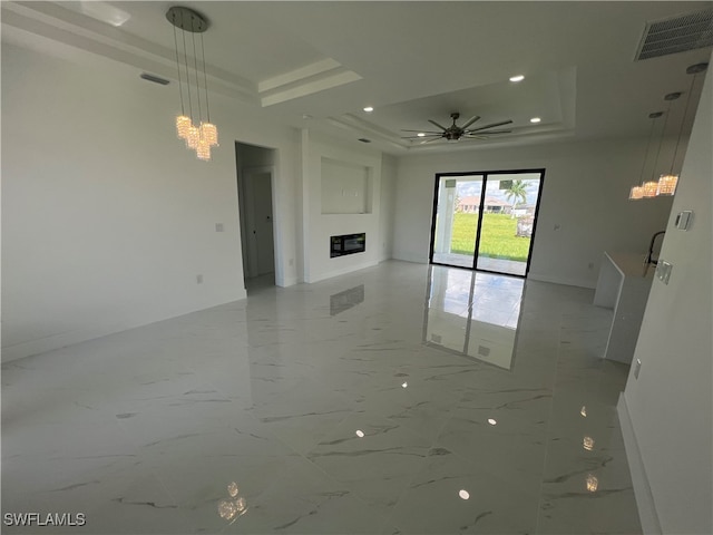 unfurnished living room with ceiling fan with notable chandelier and a tray ceiling