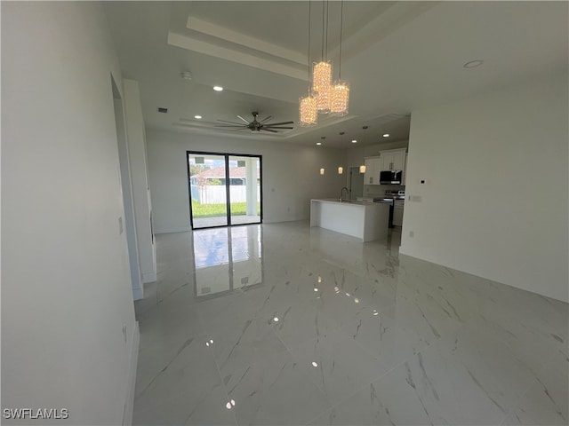 unfurnished living room with ceiling fan with notable chandelier and a tray ceiling