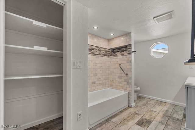 bathroom featuring hardwood / wood-style flooring, tiled shower / bath combo, a textured ceiling, and toilet