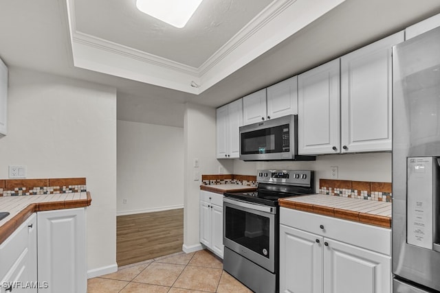 kitchen featuring appliances with stainless steel finishes, white cabinetry, ornamental molding, tile counters, and a tray ceiling