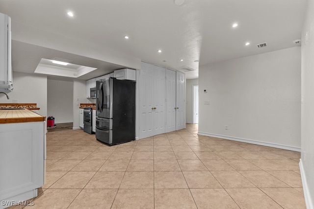 kitchen with white cabinetry, tile countertops, light tile patterned floors, appliances with stainless steel finishes, and a tray ceiling