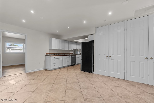 kitchen featuring light tile patterned floors, stainless steel dishwasher, white cabinets, and black fridge