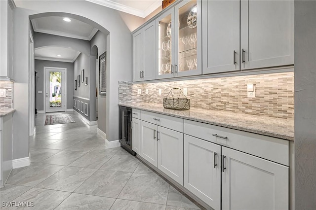 bar with light stone countertops, beverage cooler, tasteful backsplash, crown molding, and white cabinets