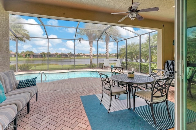 view of swimming pool with a water view, glass enclosure, ceiling fan, and a patio area