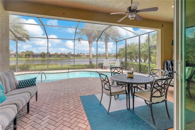 outdoor pool with ceiling fan, a lanai, a water view, and a patio