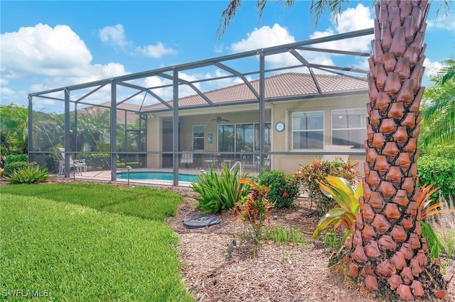 back of property with a lawn, glass enclosure, and ceiling fan