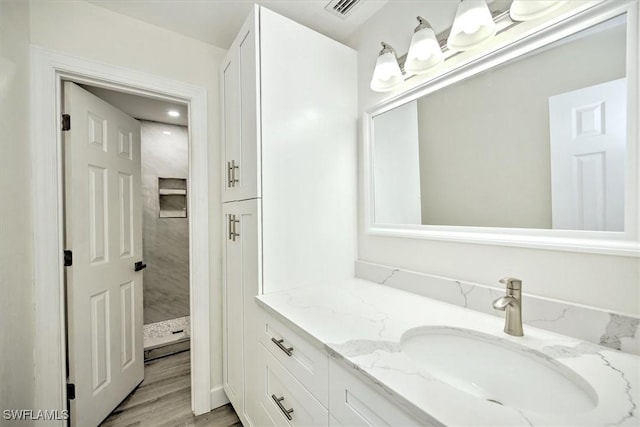 full bathroom featuring visible vents, tiled shower, vanity, and wood finished floors