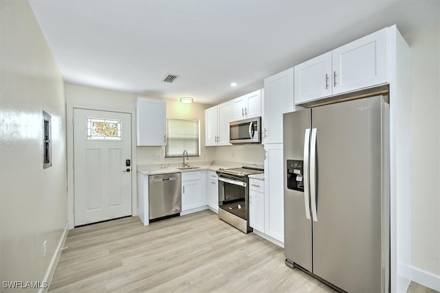 kitchen with sink, appliances with stainless steel finishes, white cabinets, and light hardwood / wood-style floors